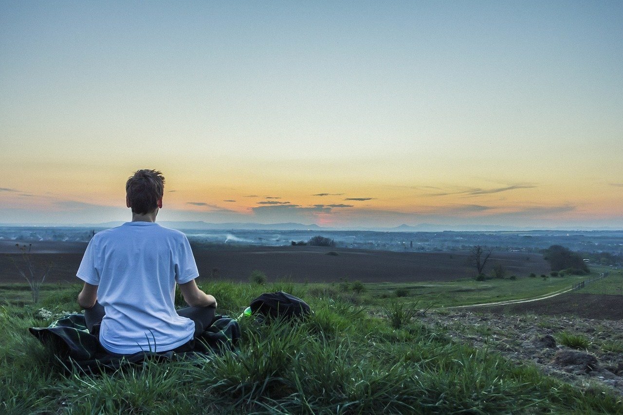A man meditating on a grassy hill at sunrise